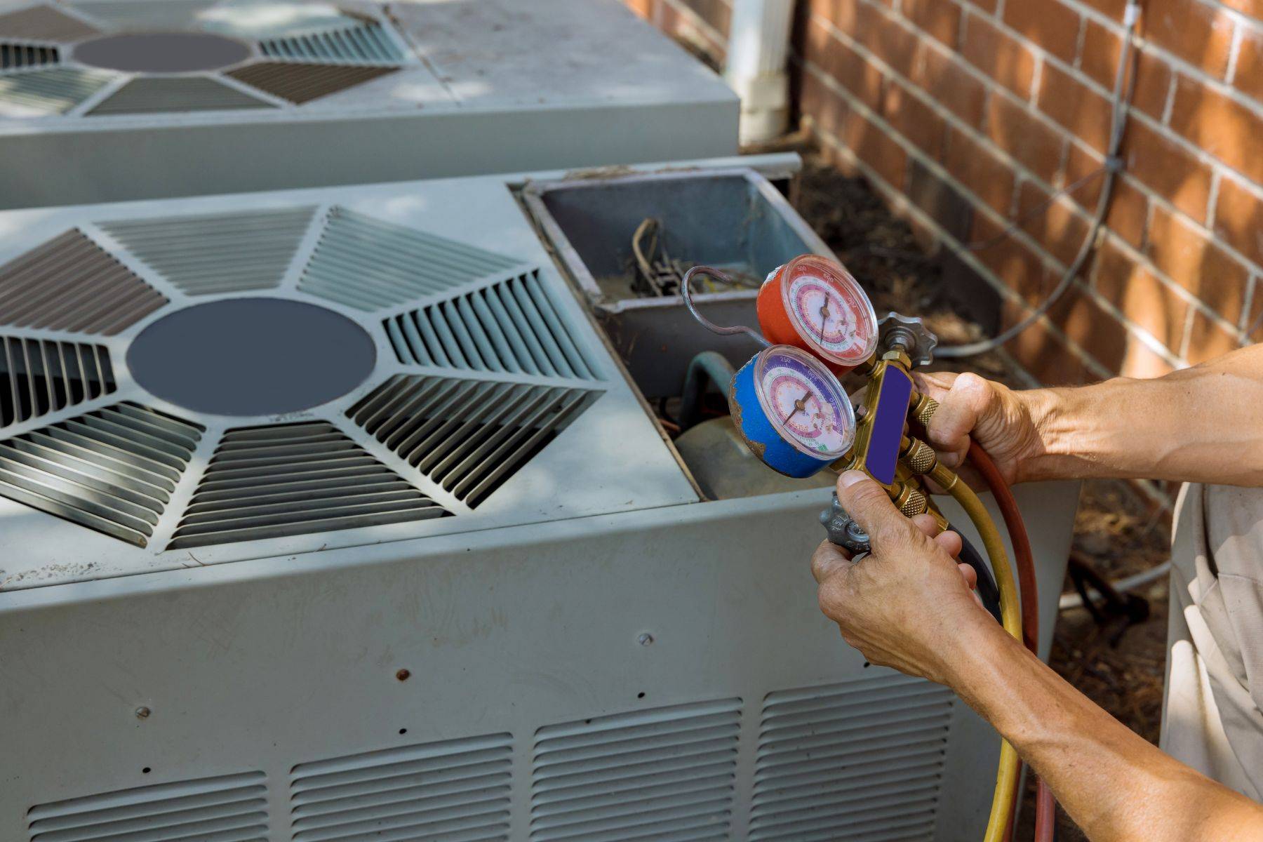 HVAC technician checking refrigerant pressures with a gauge manifold on an outdoor AC condenser